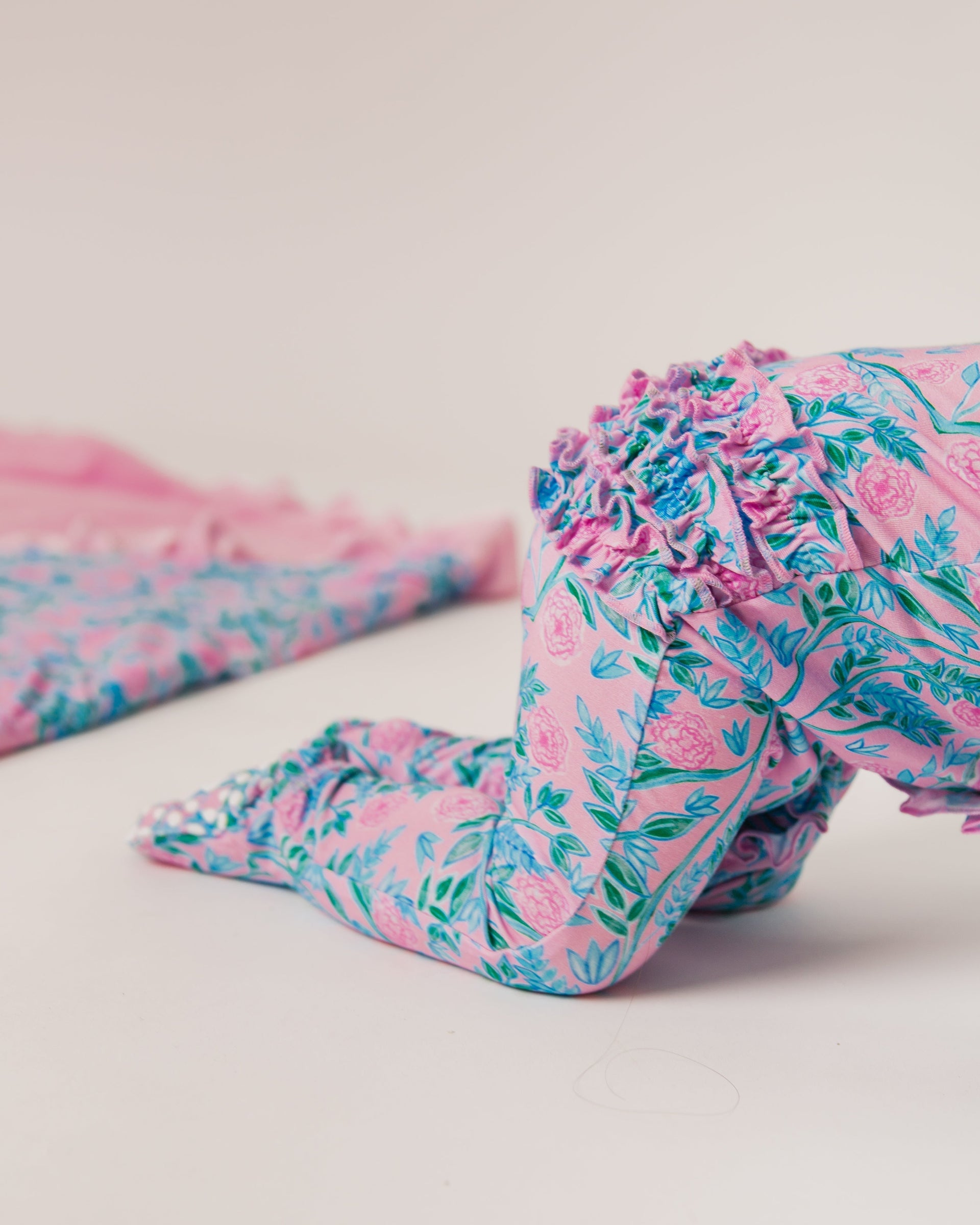 Baby's crawling legs in pink floral ruffled leggings with blue-green leaves on a pale studio background